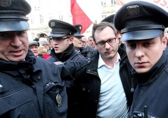 Antisemita a extremista Adam B. Bartoš putuje, kam patří - v poutech do policejní cely.