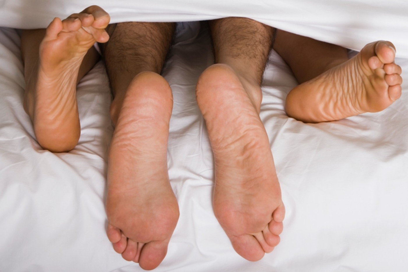 High angle view of a couple's feet under the sheets of a bed