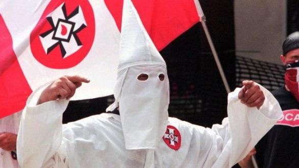 Člen KKK s vlajkou s logem Ku-klux-klanu