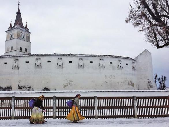 Hărman / Honigberg. Cikánky kráčející na trh podél obranné zdi kostela s nejvyšší věží ve východní části Sedmihradska (52 metrů). Uvnitř je etnografické muzeum, o které se stará dosud živá komunita zdejších Sasů. Většině je však přes 70 let...