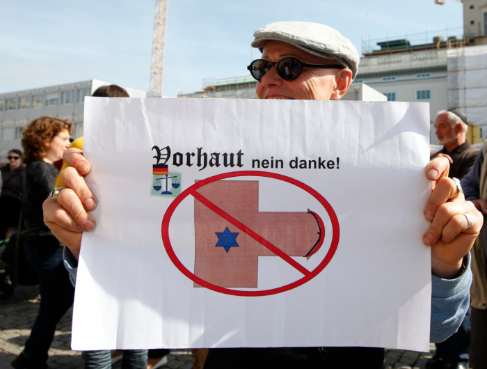 „Předkožka? Ne, děkuji.“ Nápis na transparentu z demonstrace na berlínském Bebelplatzu v září 2012. Sešlo se tu na pětset převážně židovských, ale i křesťanských a muslimských účastníků protestujících proti rozhodnutí německého soudu zákazat obřízku.
